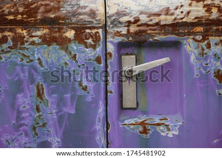 Poor quality paint on the car, cracks and scratches on the rusty metal surface. Abstract pattern, texture, pattern detail background with rusty stains. A car door handle on an old purple car