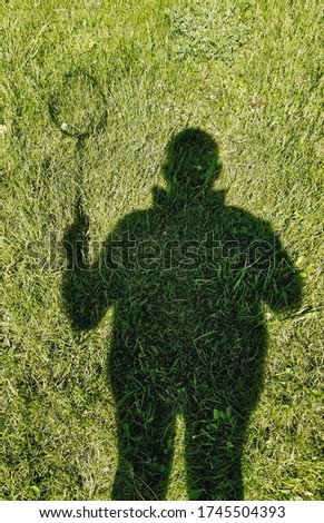 Silhouette, shadow of a man with a tennis racket on green grass, meadow in nature. Sports and recreation. Photography, concept.