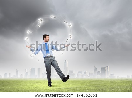 Handsome businessman juggling with question marks against city background