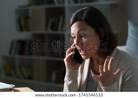 Angry middle age woman calling on smart phone sitting in the livingroom at night at home Royalty-Free Stock Photo #1745546510