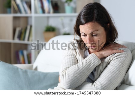 Sad pensive middle age woman looking down depresed sitting on the sofa in the living room at home Royalty-Free Stock Photo #1745547380