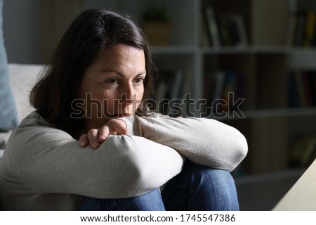 Pensive adult woman looking away thinking sitting on the floor in the livingroom at night at home Royalty-Free Stock Photo #1745547386