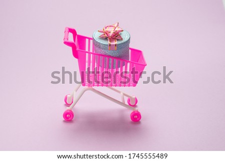 Blue present box with pink bow in a shopping cart on a pink background. 