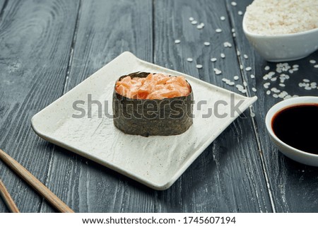 Classic japanese sushi rolls - gunkan with salmon and spicy white sauce on a white ceramic plate on a black wooden background. Close up