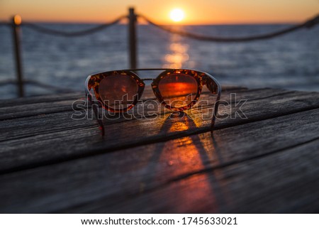 sunglasses on a wooden table during a sunset at sea