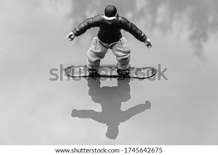 A grayscale shot of the reflection of a snowboarder figurine toy in the water