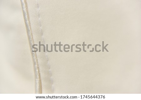 selective focus at the white stitch on the beige fabric. Copy space. Clothes manufacturing industry concept.