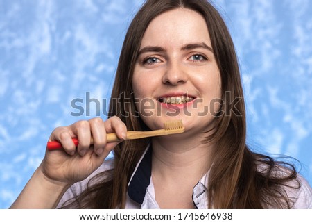 beautiful young girl with a smile holds in her hand a bamboo toothbrush in the bathroom on a blue textural background. environmentally friendly. morning hygiene concept. place for text.