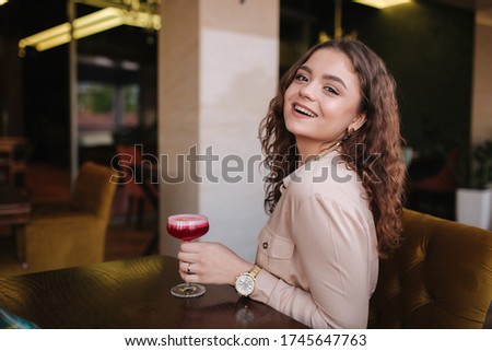Young woman sitting in restaurant and drink cocktail. Beautiful girl with curly hair smile to camera