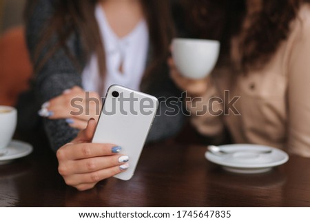 Two girls friend drink coffee in cafe and look in smat phone. Happy smiled women sittng on terrace. People look stories. Middle selection