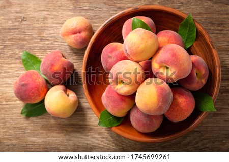 fresh ripe peaches with leaves in a bowl on a wooden table, top view Royalty-Free Stock Photo #1745699261