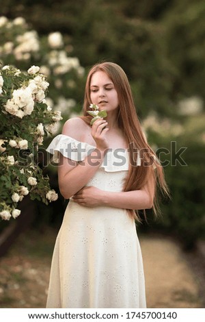 Portrait of a young girl on nature near a bush with roses.
Image with selective focus and noise effects. Focus on the girl.