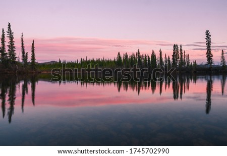 Peaceful sunset over a calm lake with a perfect reflection in the Yukon, Canada.