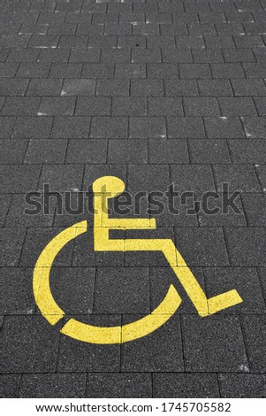 Yellow wheelchair parking sign on dark gray paving, space for copy, background