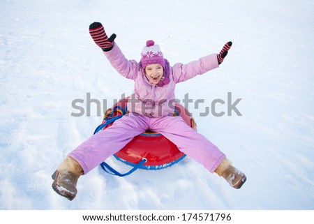 Child sledding in winter hill. Happy girl tobogganing