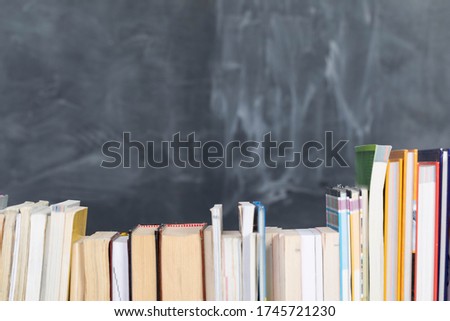 School readings. Stack of many books. A school board in the background is not thoroughly wiped with a sponge. Traces of chalk on the chalkboard.