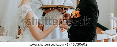 The groom puts a wedding ring on the bride’s finger and the priest reads the text from the Bible. The wedding ceremony in the church.