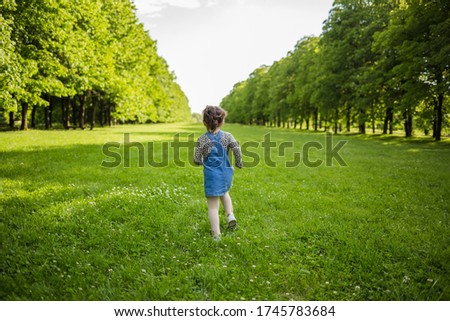 Running girl in a denim sundress in a summer meadow with lime trees. The view from the back.