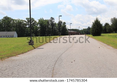 Driveway to the church, street lights on the side and home in background surrounded by a forest and loving trees 