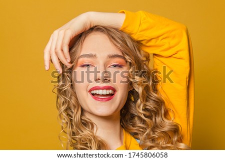 Happy woman with long curly hair smiling on bright yellow background