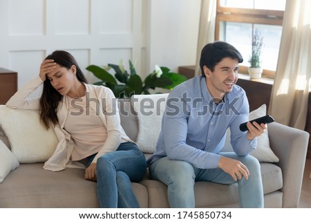 Unhappy mad young woman sit separately angry at smiling man spouse watching football match on TV, millennial caucasian couple disagreement misunderstanding on television program or channel choice Royalty-Free Stock Photo #1745850734