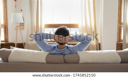 Back view of relaxed caucasian man sit rest on comfortable couch hands over head look in window distance dreaming, calm male relax on sofa in living room, enjoy home weekend, stress free concept Royalty-Free Stock Photo #1745852150