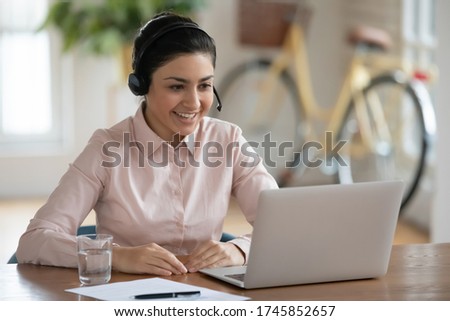 Smiling young indian female call center specialist wearing headphones with microphone, consulting clients online. Happy millennial hindu businesswoman holding video business meeting in office. Royalty-Free Stock Photo #1745852657
