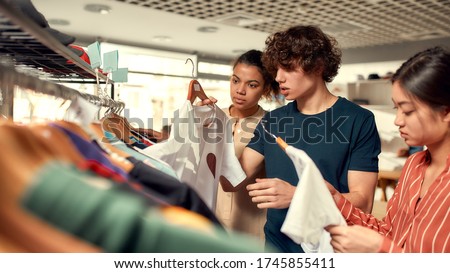 Creative people looking at already made items, while discussing logo and design of T-shirt. Young man and women at custom T-shirt, clothing printing company. Horizontal shot