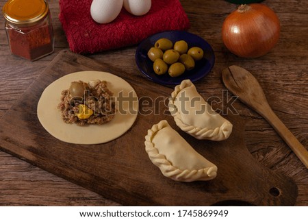 The traditional Argentine meat pie, its ingredients, meat, egg, onion, olive and condiments rustic wooden table