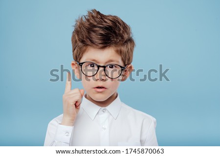 eureka, handsome little boy in glasses is surprised, inspired, I have an idea, Raise your index finger up, copy space, isolated on blue background Royalty-Free Stock Photo #1745870063