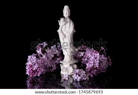 Guanyin framed by pink lilac flowers on a black background with reflection