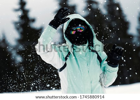 Unrecognizable portrait of snowboarder girl posing and snowy mountains in cold winter weather, wearing her googles mask, with color mirror lens.