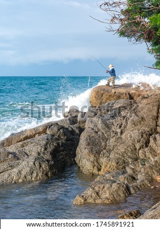 Fisherman on the background of the raging sea and waves. Splashing water around an asian fisherman fishing on the seashore on the rocks