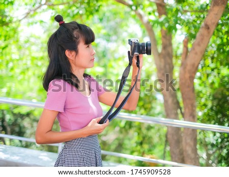 Asian woman holding mirrorless camera on blur image of evergreen forest in travel summer holidays. staff woman professional photographer with mirrorless camera  she is happy on a holiday.