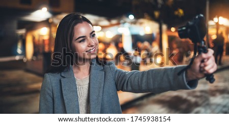 Female vlogger recording with digital camera. Smiling woman taking selfie video on light night city. Traveler making video for her blog. Vlogger uses photo technology for shoot social media