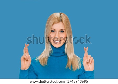 portrait of a young pretty happy woman crossing fingers wishing, praying, christening. isolated on blue color background. Positive emotions facial expression feelings