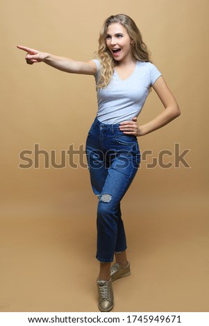 Image of happy young woman standing isolated over beige wall background. Looking camera showing copyspace pointing.