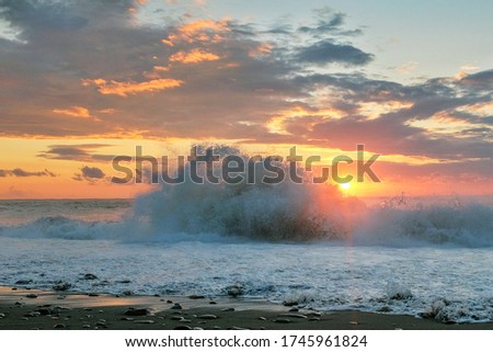 View of the black sea waves splashing on the coast with beautiful sunset cloudy sky background 