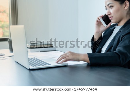 A girl businessman is talking on the phone with a smile while sitting at a desk and opening a modern working laptop in the office.