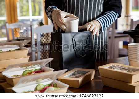Restaurant worker wearing protective mask and gloves packing food boxed take away. Food delivery services and Online contactless food shopping.
 Royalty-Free Stock Photo #1746027122