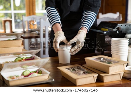 Restaurant worker wearing protective mask and gloves packing food boxed take away. Food delivery services and Online contactless food shopping.
 Royalty-Free Stock Photo #1746027146