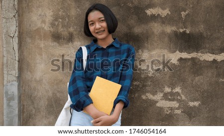 Happy Asian girl hold book and canvas bag with old wall background at school.