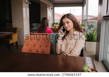 Young woman sitting on terrace and call to boyfriend. Beautiful girl with curly hair. Woman alone