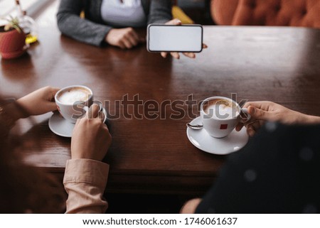 Middle selection of woman show photo in smartphone. First person view. Mock up. People drink cappuccino