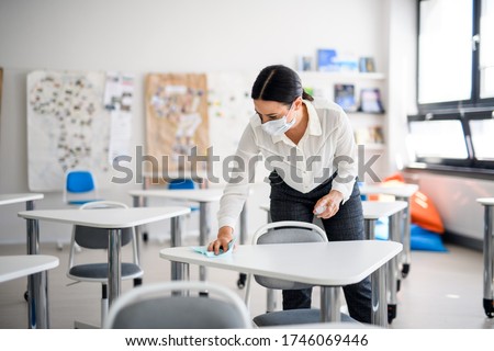 Teacher back at school after covid-19 quarantine and lockdown, disinfecting desks. Royalty-Free Stock Photo #1746069446