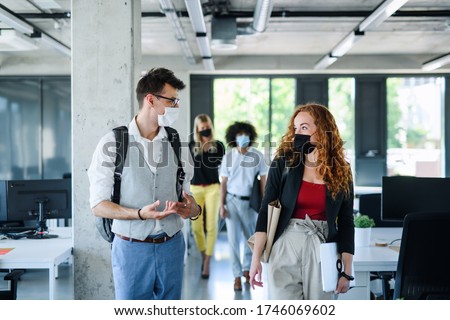 Young people with face masks back at work in office after lockdown, talking. Royalty-Free Stock Photo #1746069602