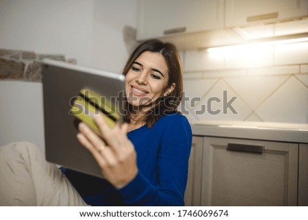 Smiling housewife in her kitchen doing online shopping with tablet. Holding credit card for easy internet payment. Home banking and technology concept.