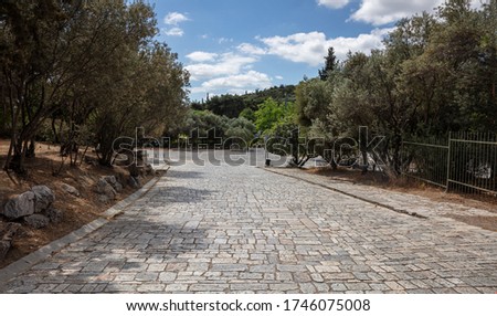 Athens, Greece. Cobblestone pathway from Acropolis to Areopagitou street, Greek flora, blue cloudy sky in a sunny spring day. Royalty-Free Stock Photo #1746075008