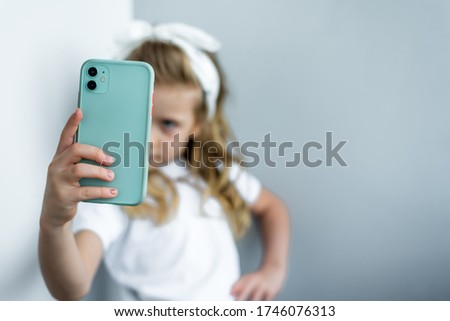 a green mobile phone in the foreground in a little girl's hands in blur in the background. Girl makes a beaf