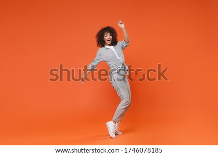 Funny young african american woman girl in gray casual clothes posing isolated on orange background in studio. People lifestyle concept. Mock up copy space. Dancing, standing on toes, rising hands Royalty-Free Stock Photo #1746078185